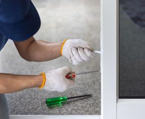 Man crouched holding a screwdriver adjusting uPVC door hinge